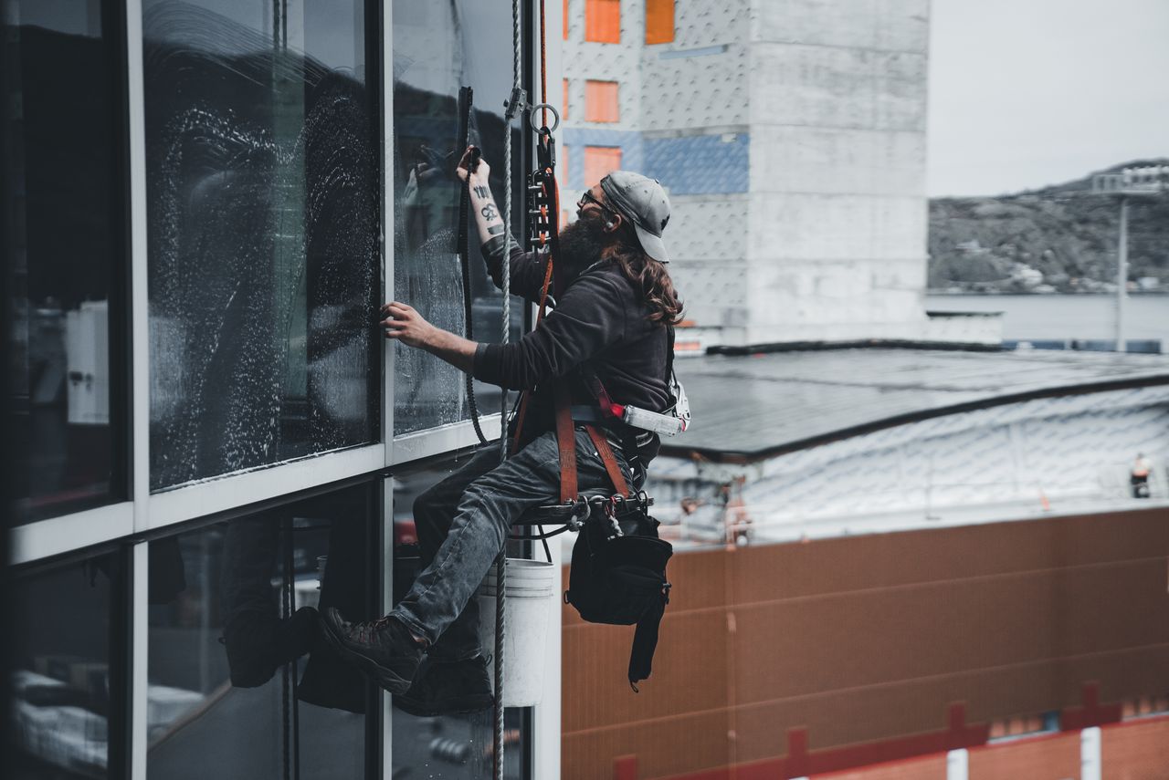 services-06 A man cleaning skyscraper windows with a harness, showcasing urban high-rise work.